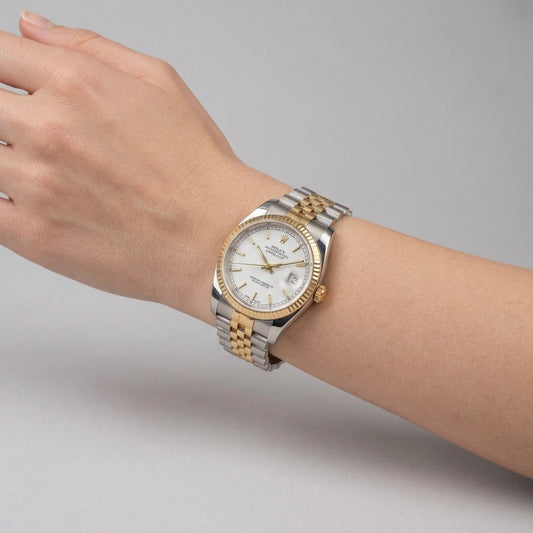 A two-tone stainless steel and gold wristwatch with a white dial, worn on a person's wrist against a neutral gray background.