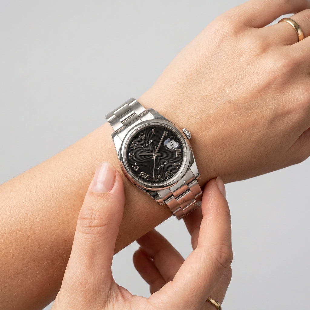 A silver stainless steel wristwatch with a black dial and date window, shown worn on a person's wrist with hands adjusting it, against a light gray background.