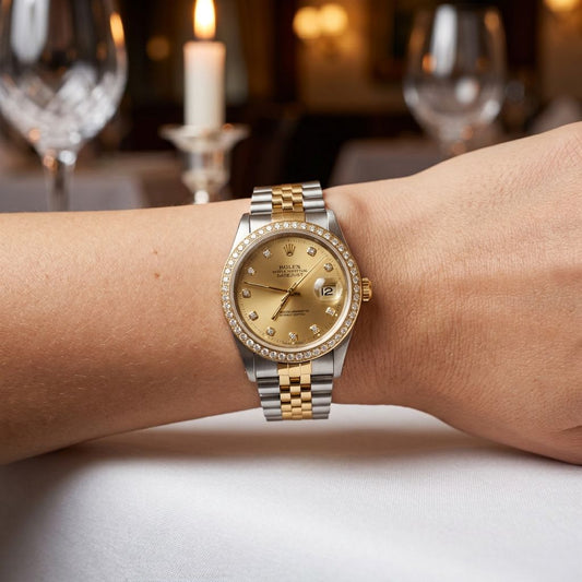 A Rolex Datejust watch with a gold dial and two-tone steel and gold Oyster bracelet, worn on a person's wrist in a softly blurred restaurant setting.