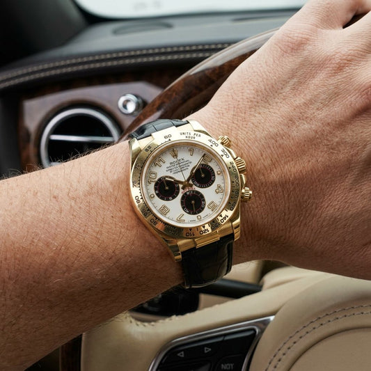 A gold-tone wristwatch with a white dial and black subdials, worn on a person's wrist inside a car.