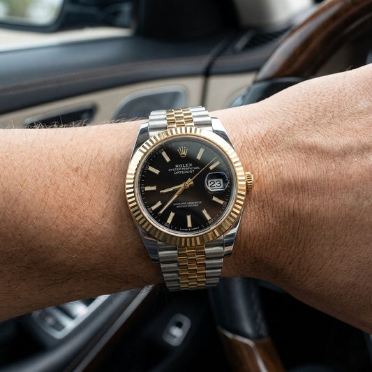 A Rolex Oyster Perpetual Datejust watch with a two-tone silver and gold bracelet and a black dial, shown worn on a person's wrist inside a car.