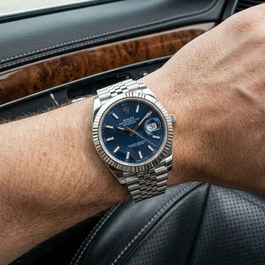 A Rolex Oyster Perpetual Datejust watch with a blue dial and silver fluted bezel and bracelet, worn on a person's wrist inside a car.