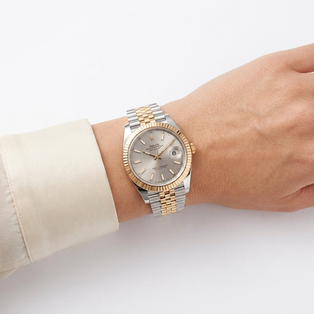 A two-tone stainless steel and gold wristwatch with a silver dial, worn on a person's wrist. The watch features a fluted gold-tone bezel and a two-tone link bracelet, with a cream-colored dress shirt cuff visible on the left.