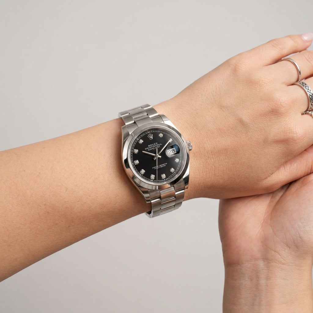 A stainless steel wristwatch with a black dial and date window, worn on a person's wrist against a plain light gray background.