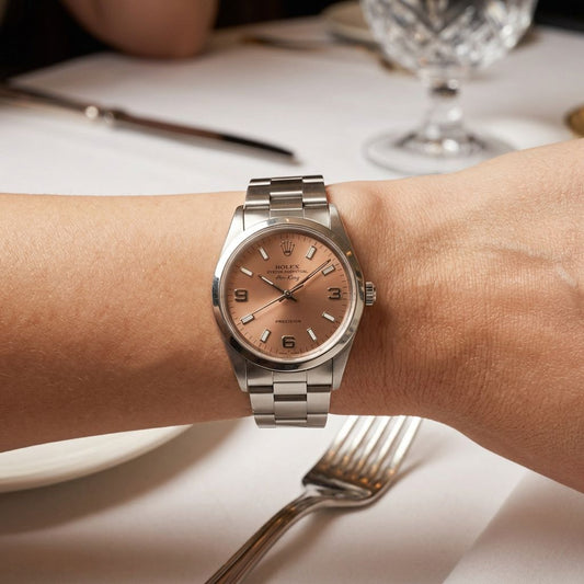 A Rolex wristwatch with a stainless steel Oyster bracelet and a champagne dial, shown worn on a person's wrist in a restaurant setting.
