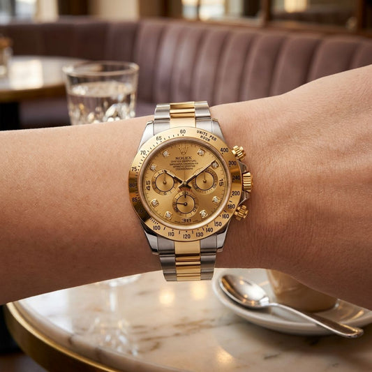 A two-tone gold and silver Rolex Daytona watch worn on a person's wrist in a cafe setting.