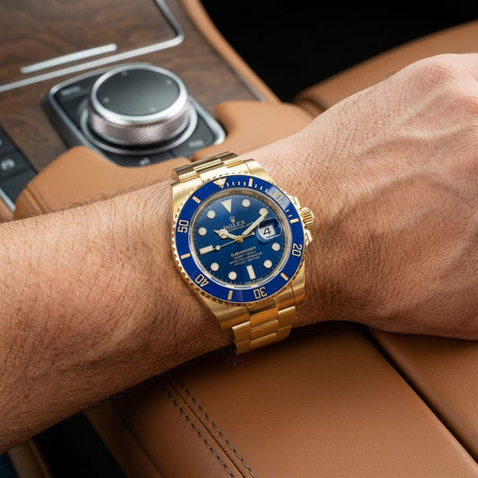 A gold-tone Rolex Submariner watch with a blue bezel and dial, worn on a person's wrist inside a car with brown leather interior.