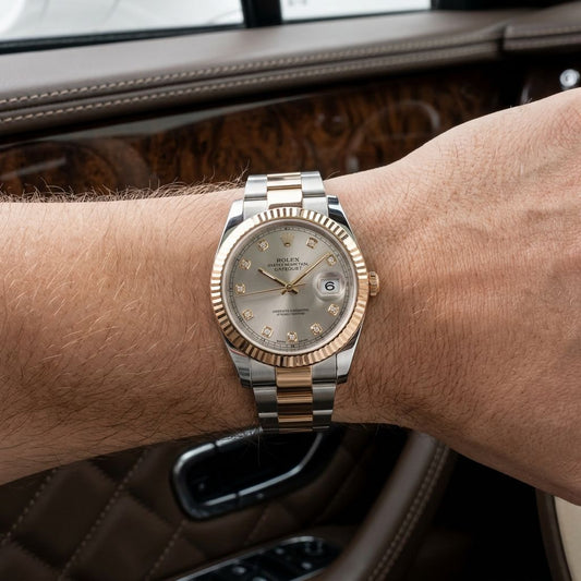 A Rolex Oyster Perpetual Datejust watch with a two-tone yellow gold and stainless steel bracelet, featuring a champagne dial and fluted bezel, shown on a person's wrist inside a car.