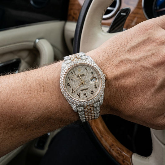 A close-up of a wrist wearing a luxury watch encrusted with diamonds, set against the interior of a car with a beige leather steering wheel and wood trim.