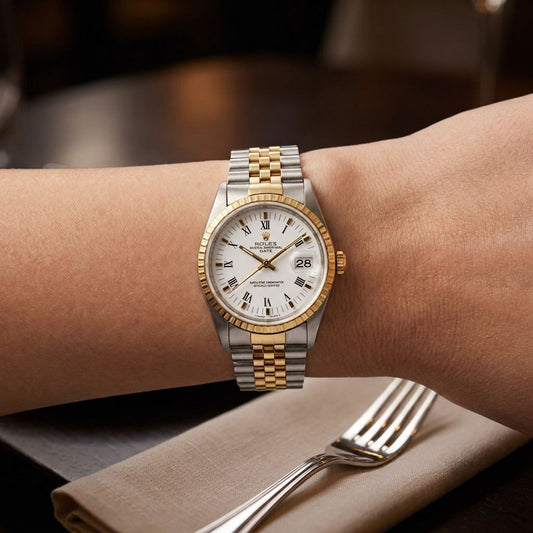 A two-tone Rolex wristwatch with a silver and gold metal bracelet, gold bezel, and white dial, shown worn on a person's wrist in a restaurant setting with a fork and napkin visible.