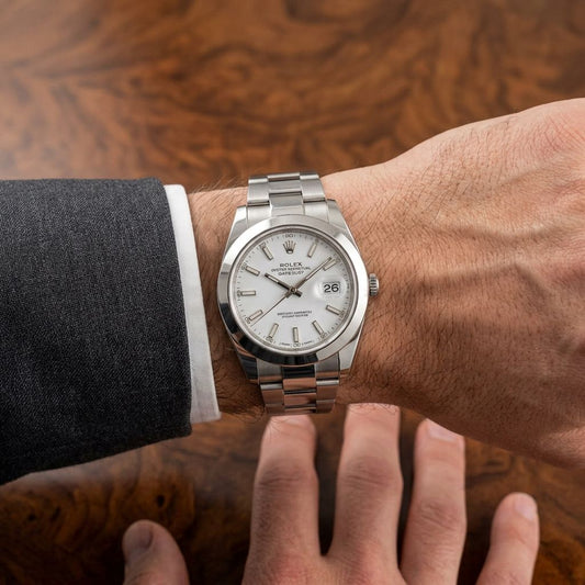 A Rolex Oyster Perpetual watch with a silver stainless steel case, white dial, and silver Oyster bracelet, shown worn on a wrist with a dark gray suit sleeve visible.