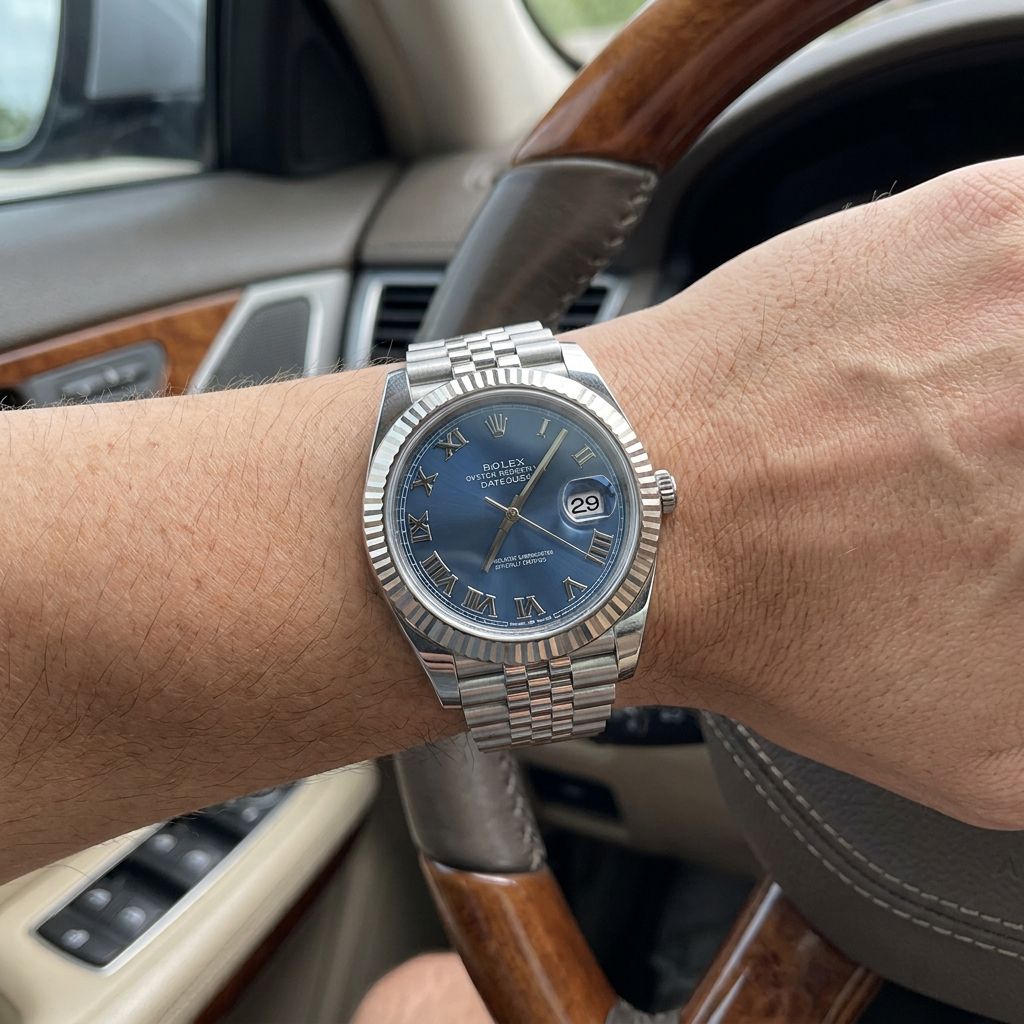 A silver Rolex Oyster Perpetual watch with a blue dial and Roman numeral hour markers, worn on a person's wrist inside a car.